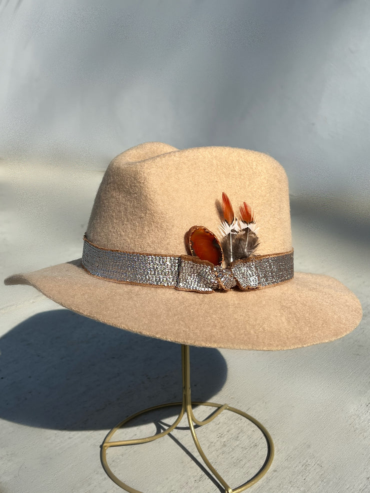 Light beige wool fedora hat with frayed metal silver band and brown underlay.  Red agate stone and brown, white and orange feathers attached as well as gold Elemant metal logo on back.