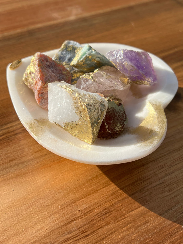 Onyx bowl with 7 different meditation stones inside. White Quartz, Rose Quartz, Green Quartz, Blue Quartz, Red Jasper, Amethyst and Orange Calcite. A gold Elemant logo emblem is attached to the bowl and both the bowl and stones are artfully gold dusted. Includes a note describing each of the meditation stones meaning and benefits.