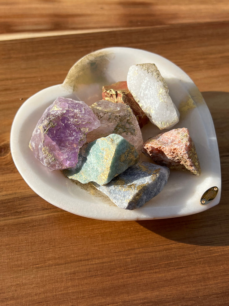 Onyx bowl with 7 different meditation stones inside. White Quartz, Rose Quartz, Green Quartz, Blue Quartz, Red Jasper, Amethyst and Orange Calcite. A gold Elemant logo emblem is attached to the bowl and both the bowl and stones are artfully gold dusted. Includes a note describing each of the meditation stones meaning and benefits.