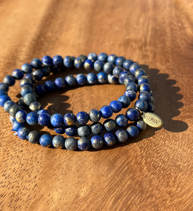 Lightly gold dusted natural Lapis Lazuli beaded bracelets on three stretchy strings of beads with an Elemant logo emblem attached to one of them. 