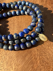 Lightly gold dusted natural Lapis Lazuli beaded bracelets on three stretchy strings of beads with an Elemant logo emblem attached to one of them.
