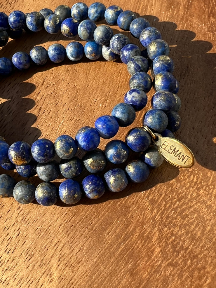 Lightly gold dusted natural Lapis Lazuli beaded bracelets on three stretchy strings of beads with an Elemant logo emblem attached to one of them.