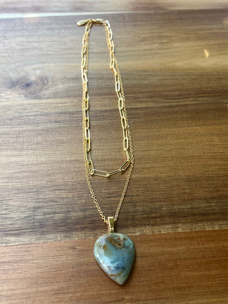 Opal pendant with layered 14k gold filled chains. An oval long chained link and a thinner longer gold chain that the Opal hangs from. A gold Elemant logo emblem is attached at the clasp. Opal is the stone of abundance, fortune, luck, health and wealth.