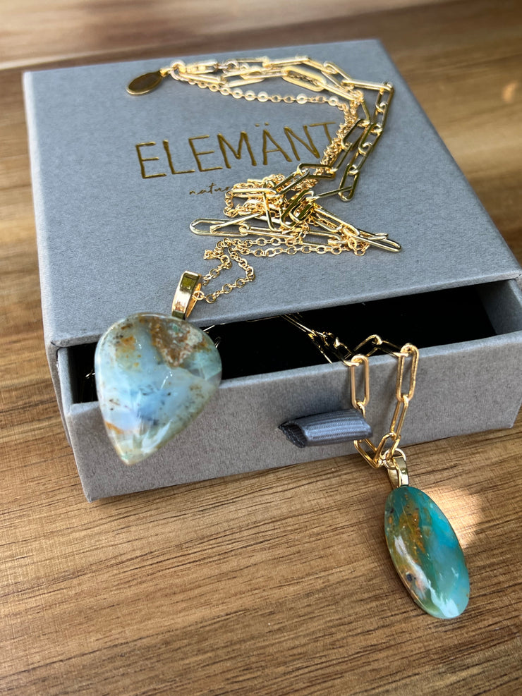 Opal pendant with layered 14k gold filled chains. An oval long chained link and a thinner longer gold chain that the Opal hangs from. A gold Elemant logo emblem is attached at the clasp. Opal is the stone of abundance, fortune, luck, health and wealth.
